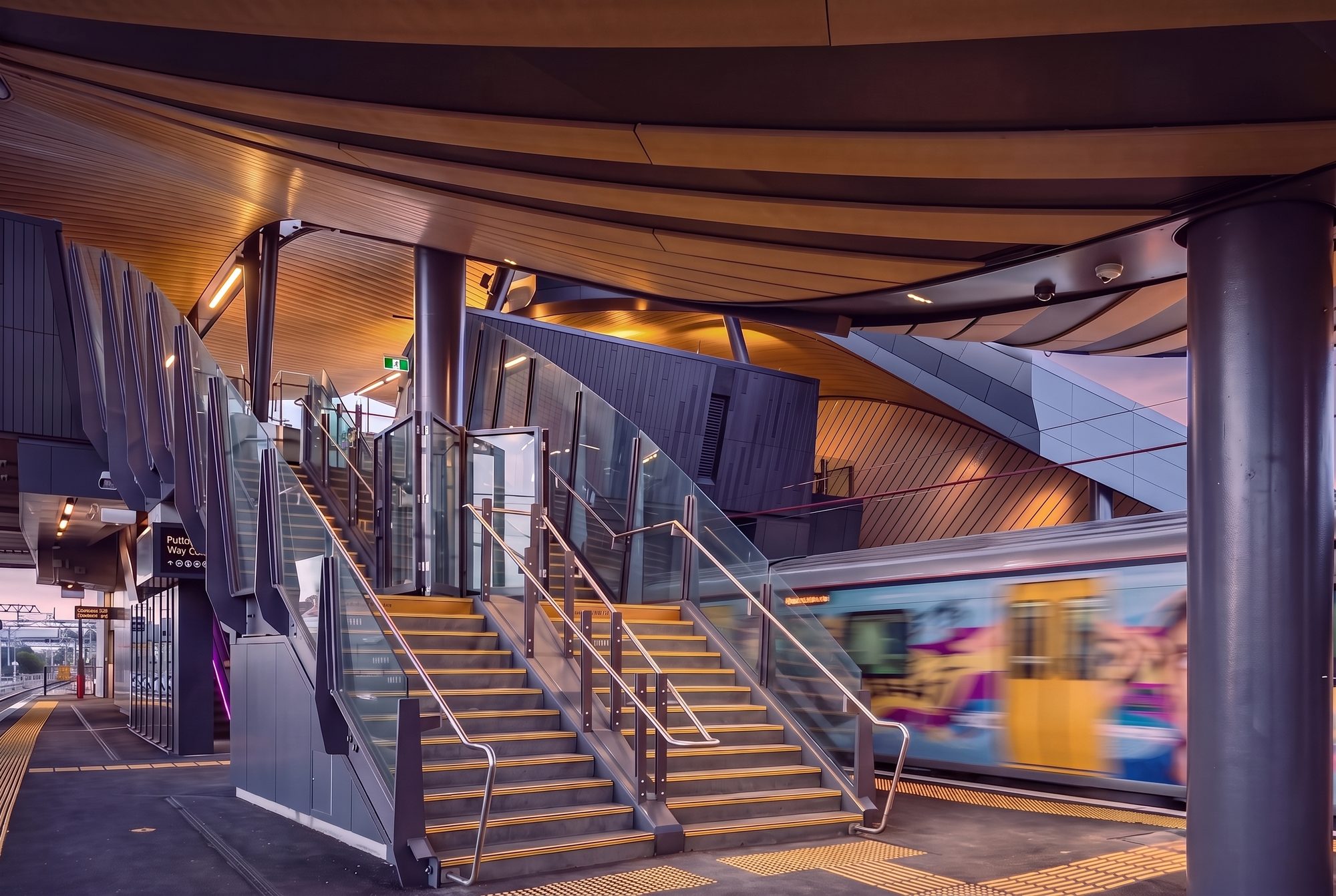 Platform and stairs at Puhinui Station, with a train arriving